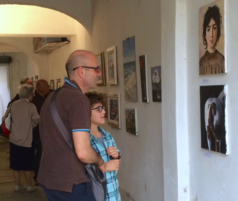 Padre e figlio ammirano quadri alla mostra di fine anno degli allievi del Atelier di pittura a Firenze